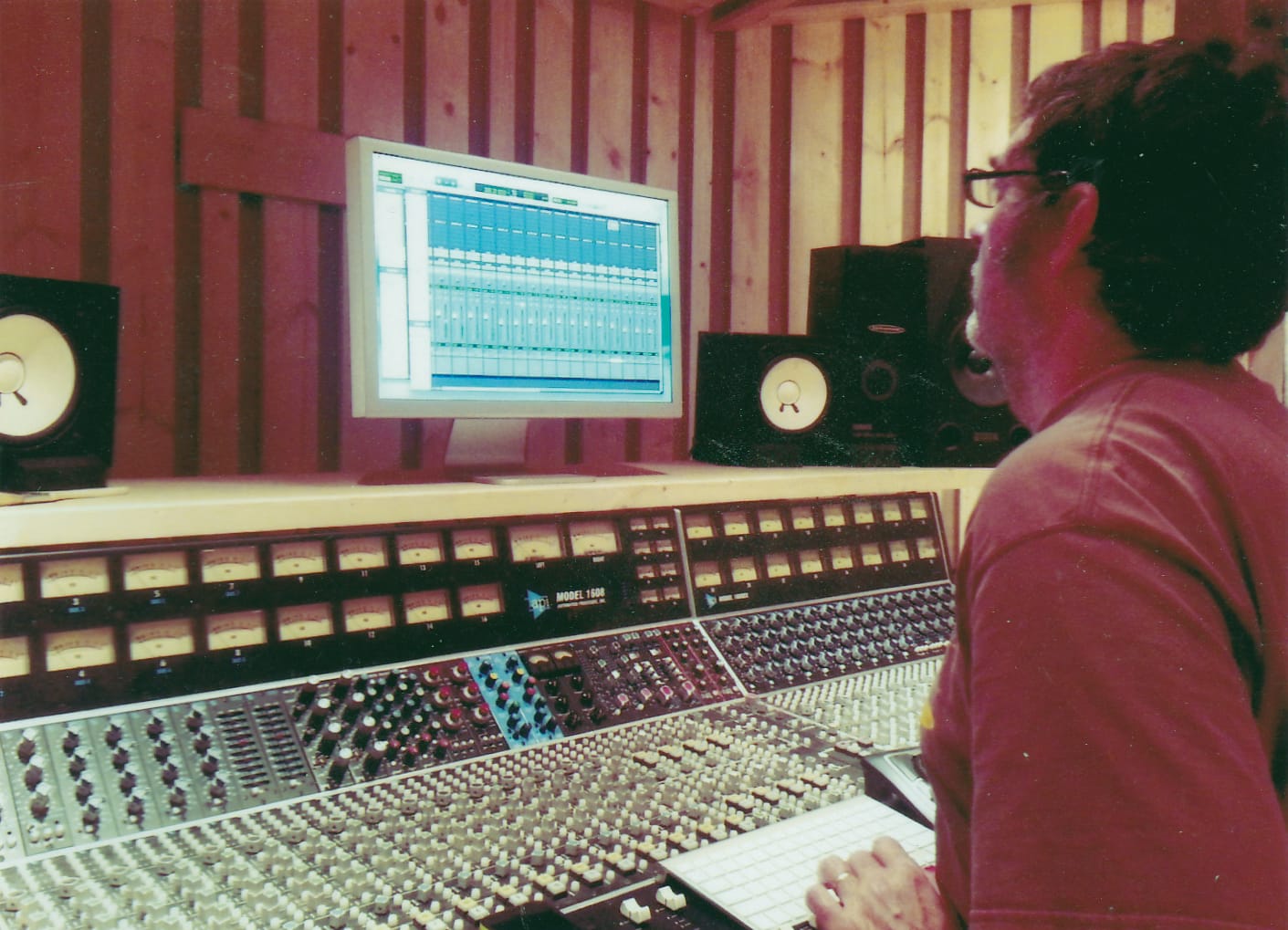 a man in a red shirt sits at a mixing board in a studio