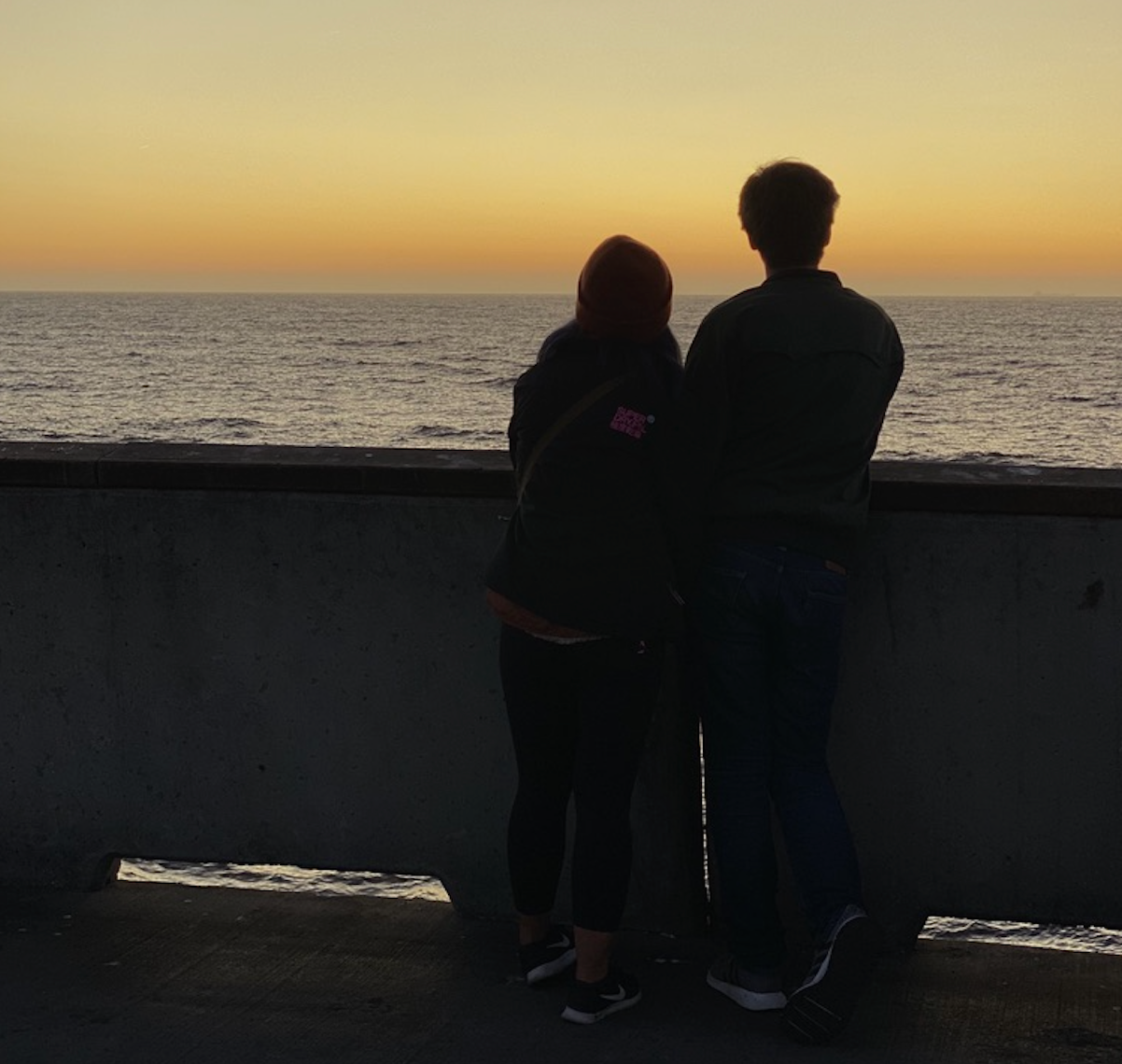 a couple stands on Pacifica Pier, silhouetted by the sunset