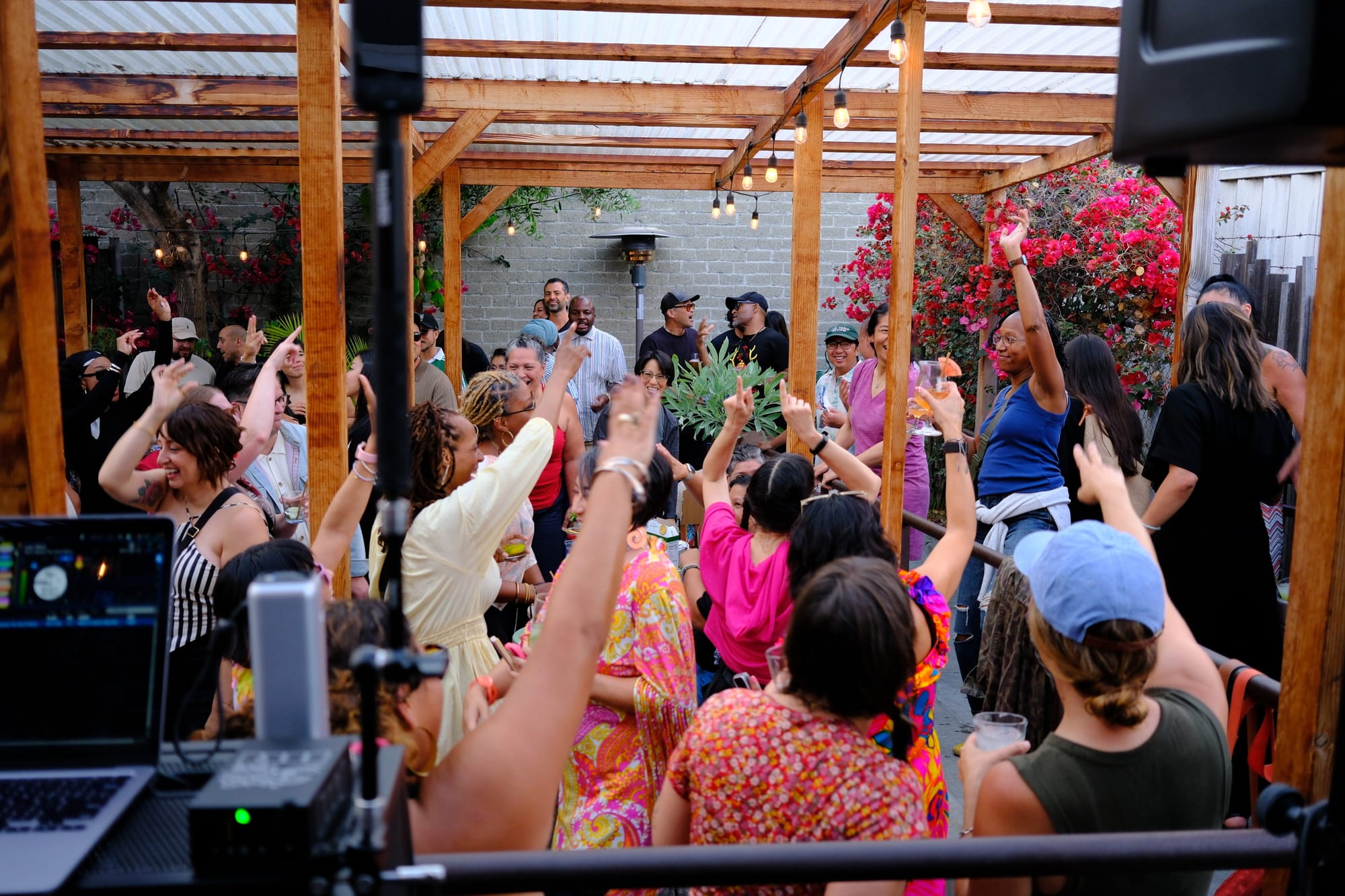 A crowd of brightly-dressed millennials and Gen Xers dance with their arms in the air.
