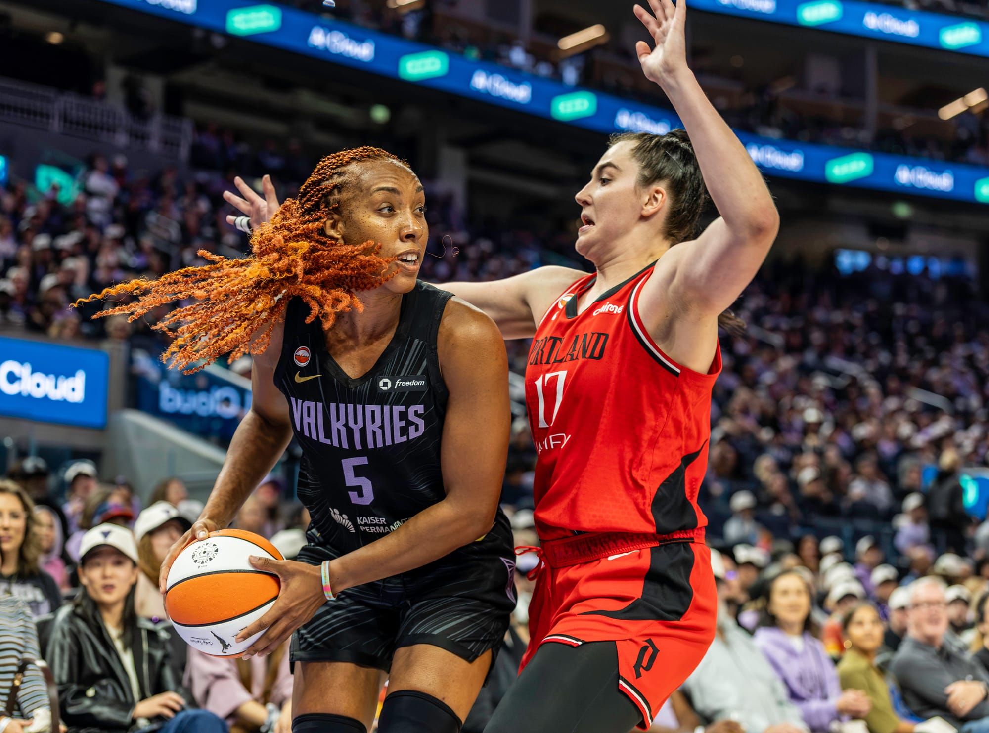 WNBA player in black uniform holding a basketball while being guarded by a player in a red uniform