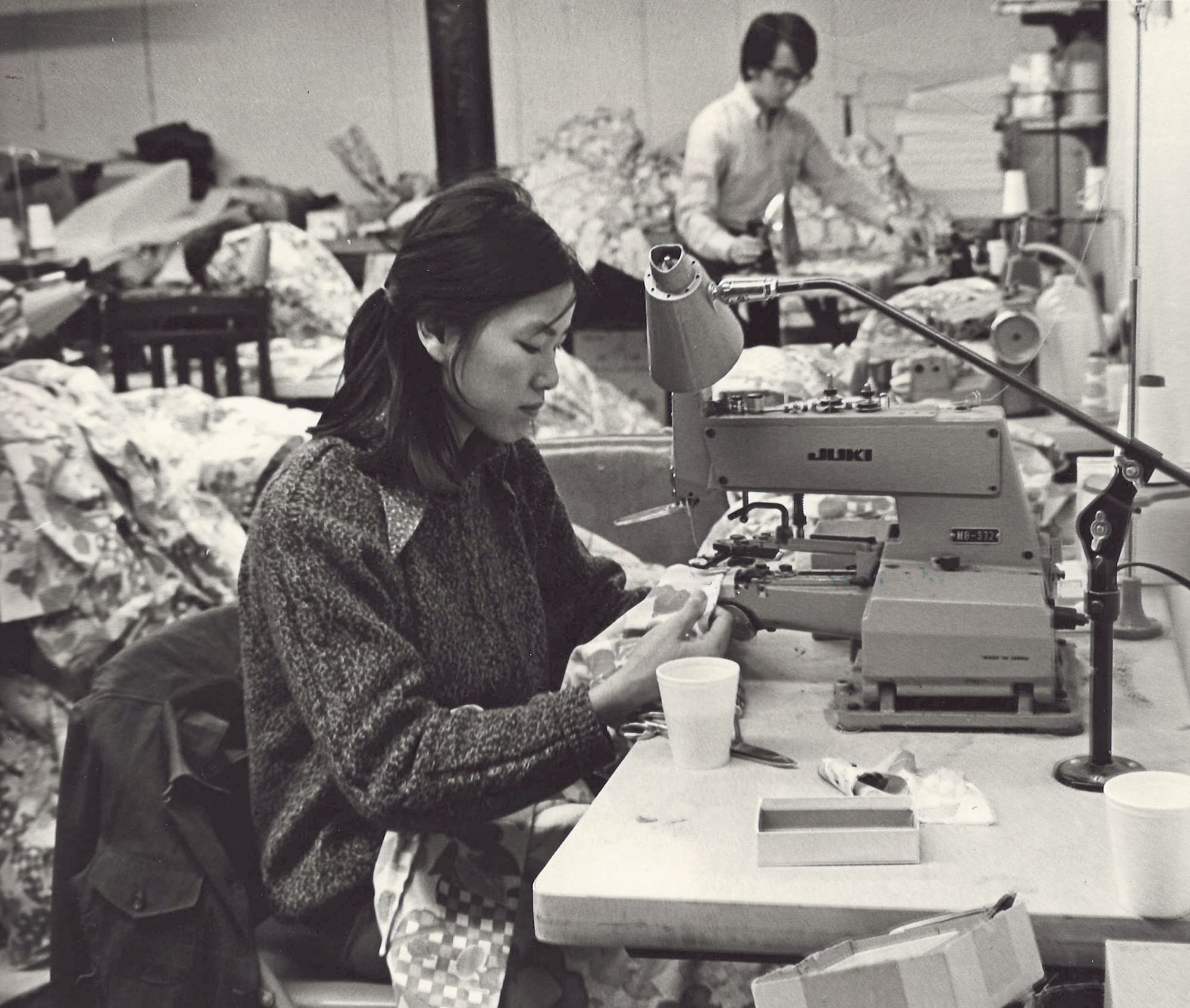 A woman focusing on her work at a sewing machine inside of a facility filled with fabric.