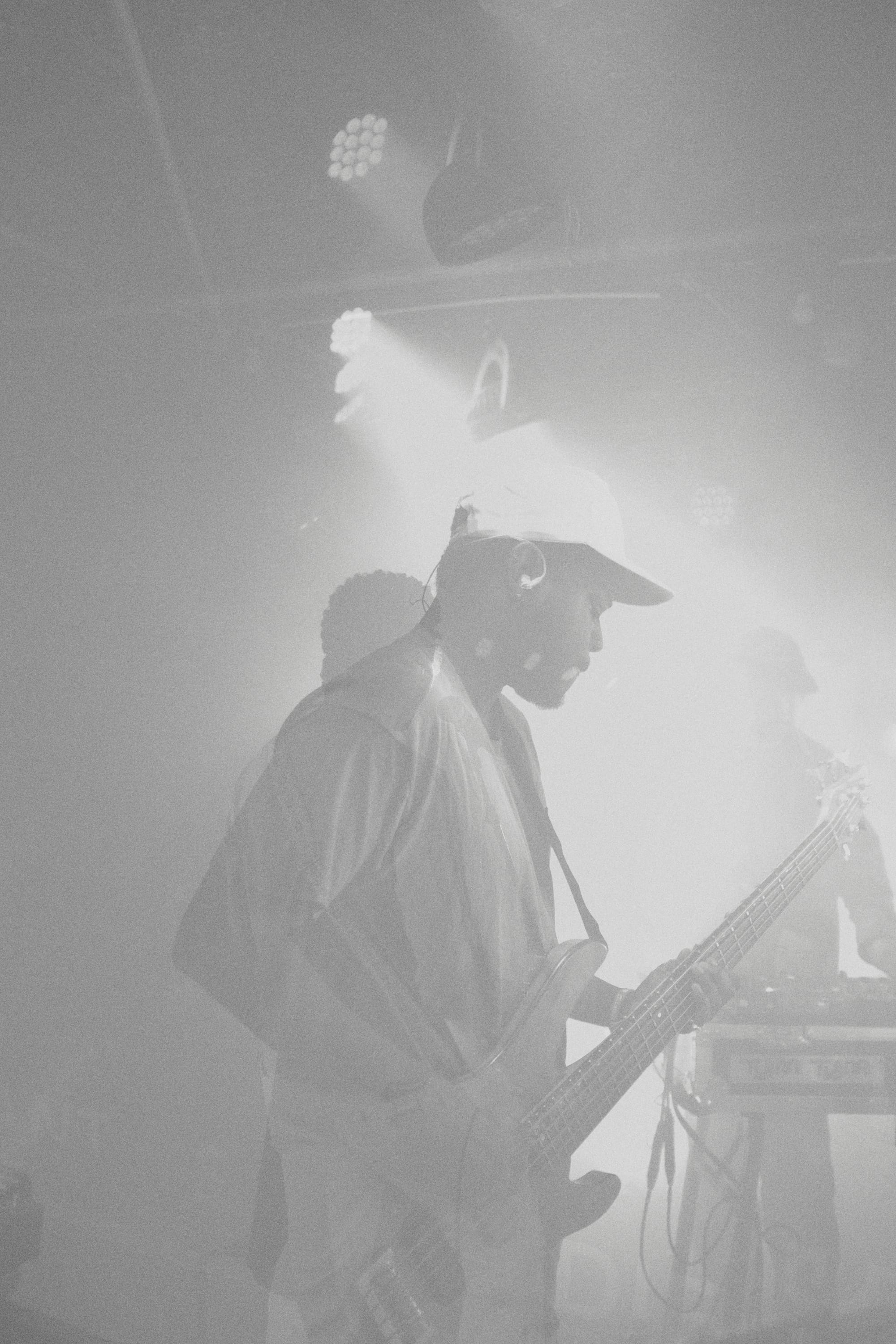 a washed-out black and white image of a person in a ball cap playing bass