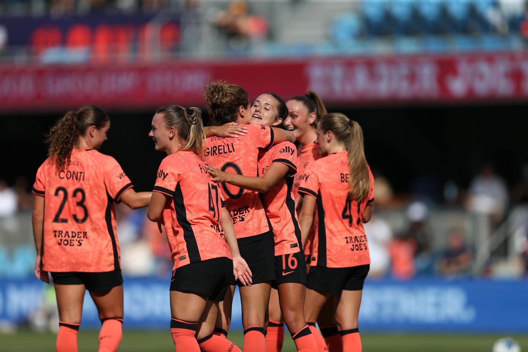 a group of six women in orange and black soccer jerseys embrace on a field