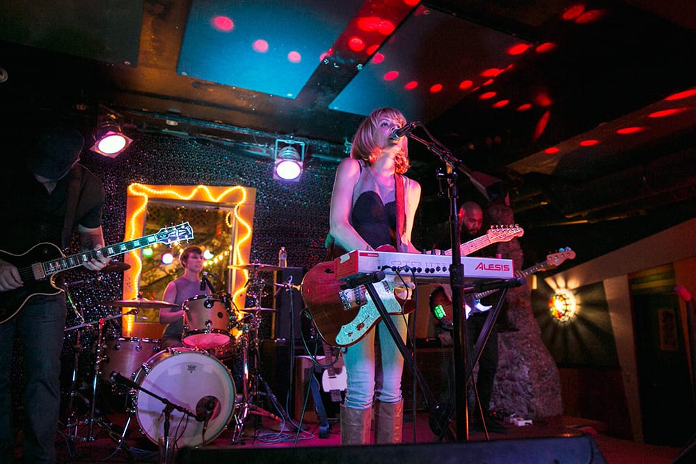 a pop band with a blonde singer and guitarist on stage at a rock club