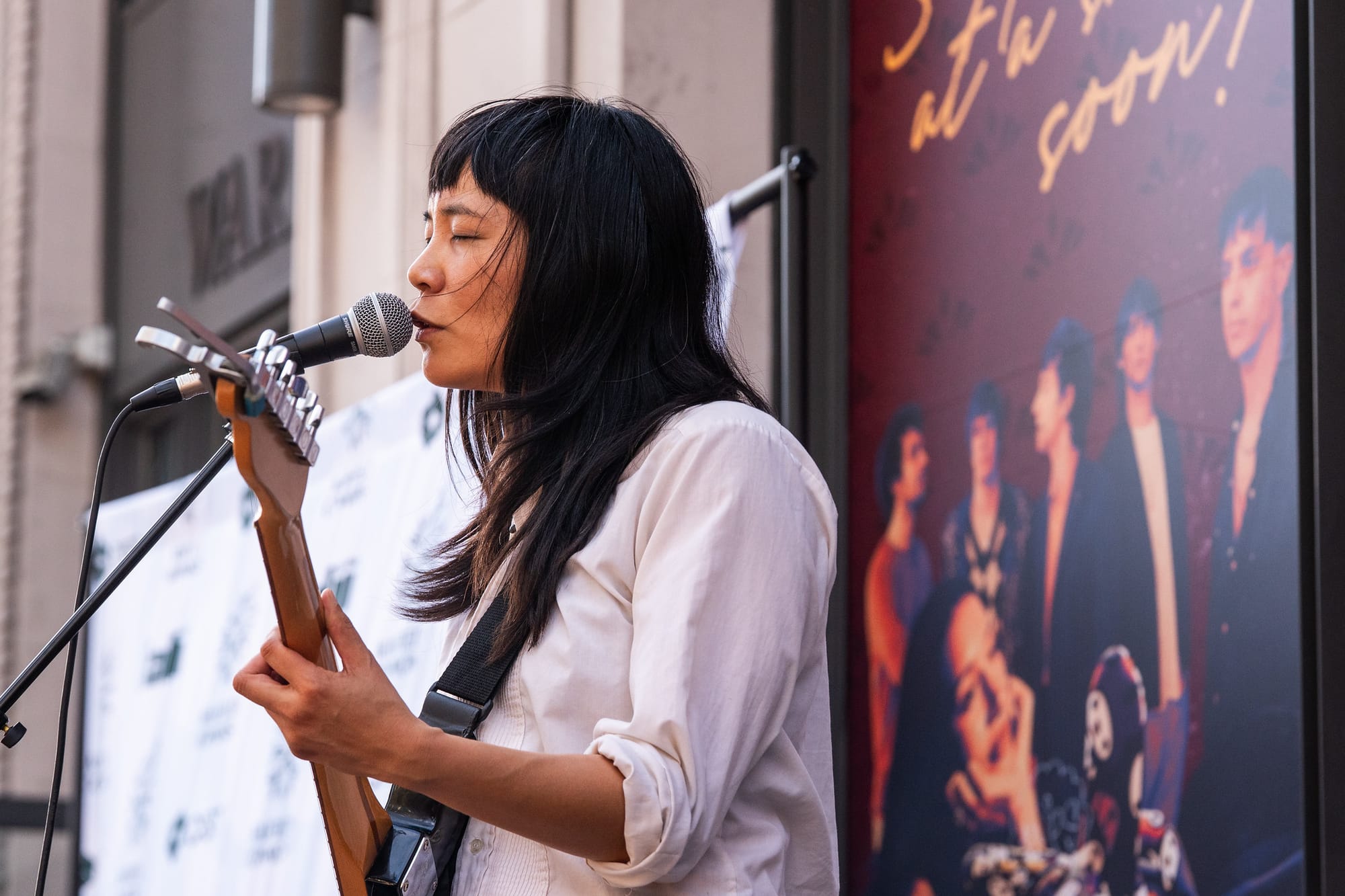Woman in white shirt singing into a microphone while playing guitar.