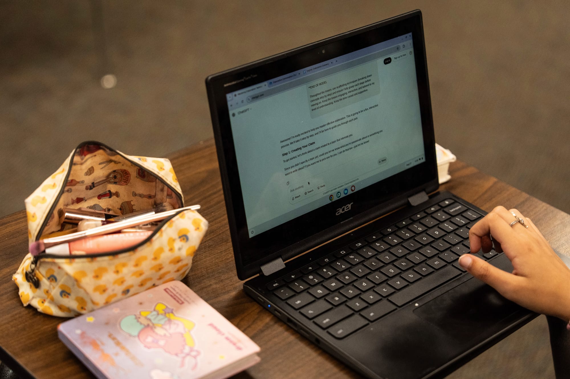 a chromebook is shown with a person's hand hovering over it, next to a makeup case on a desk