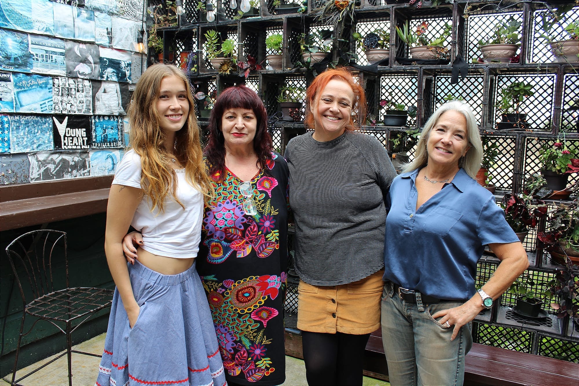 Four women ranging from their 20s to their 60s pose smiling on the back patio at a music venue
