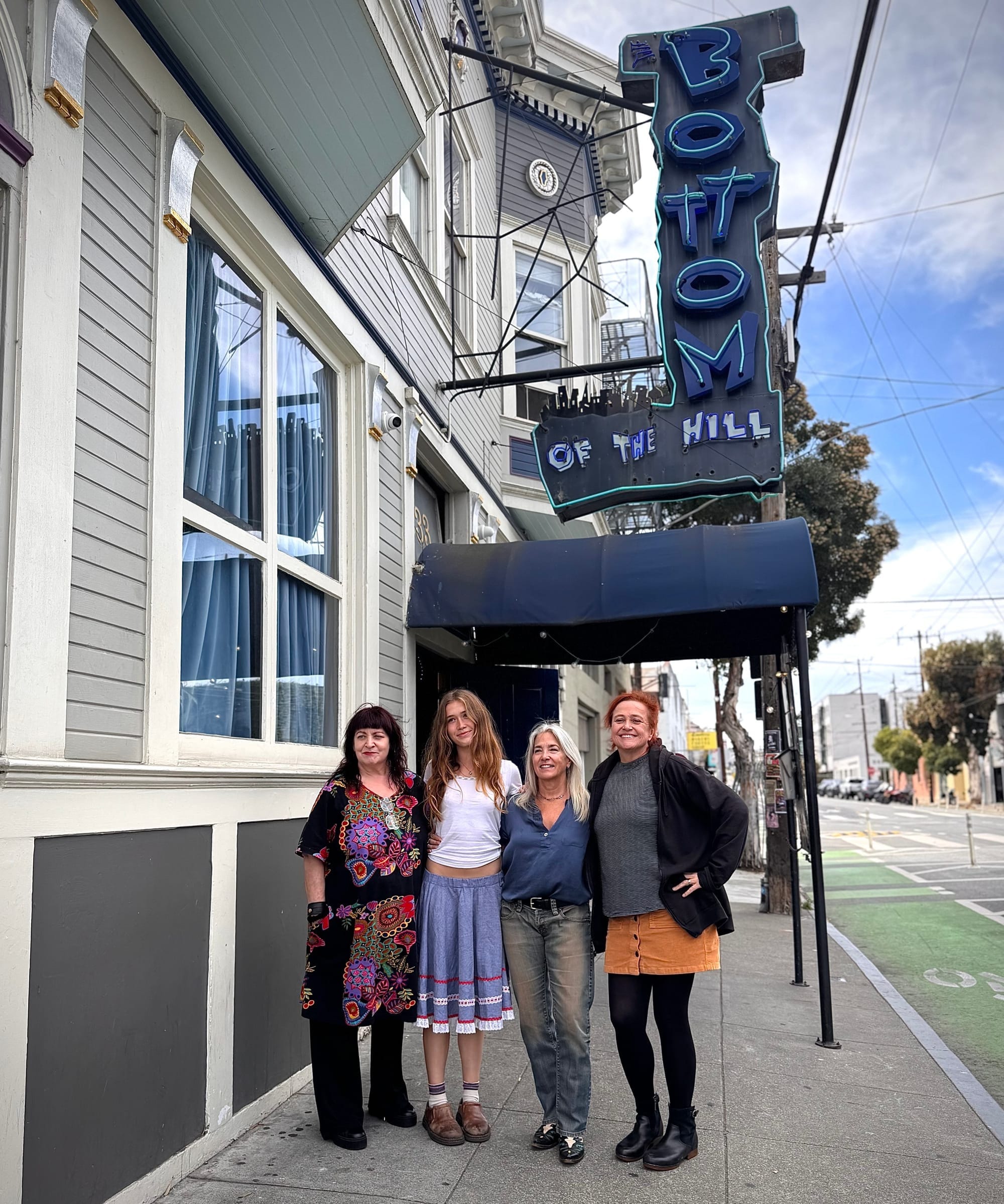 four women stand on the sidewalk in front of Bottom of the Hill, ages ranging from early 20s to mid-60s.