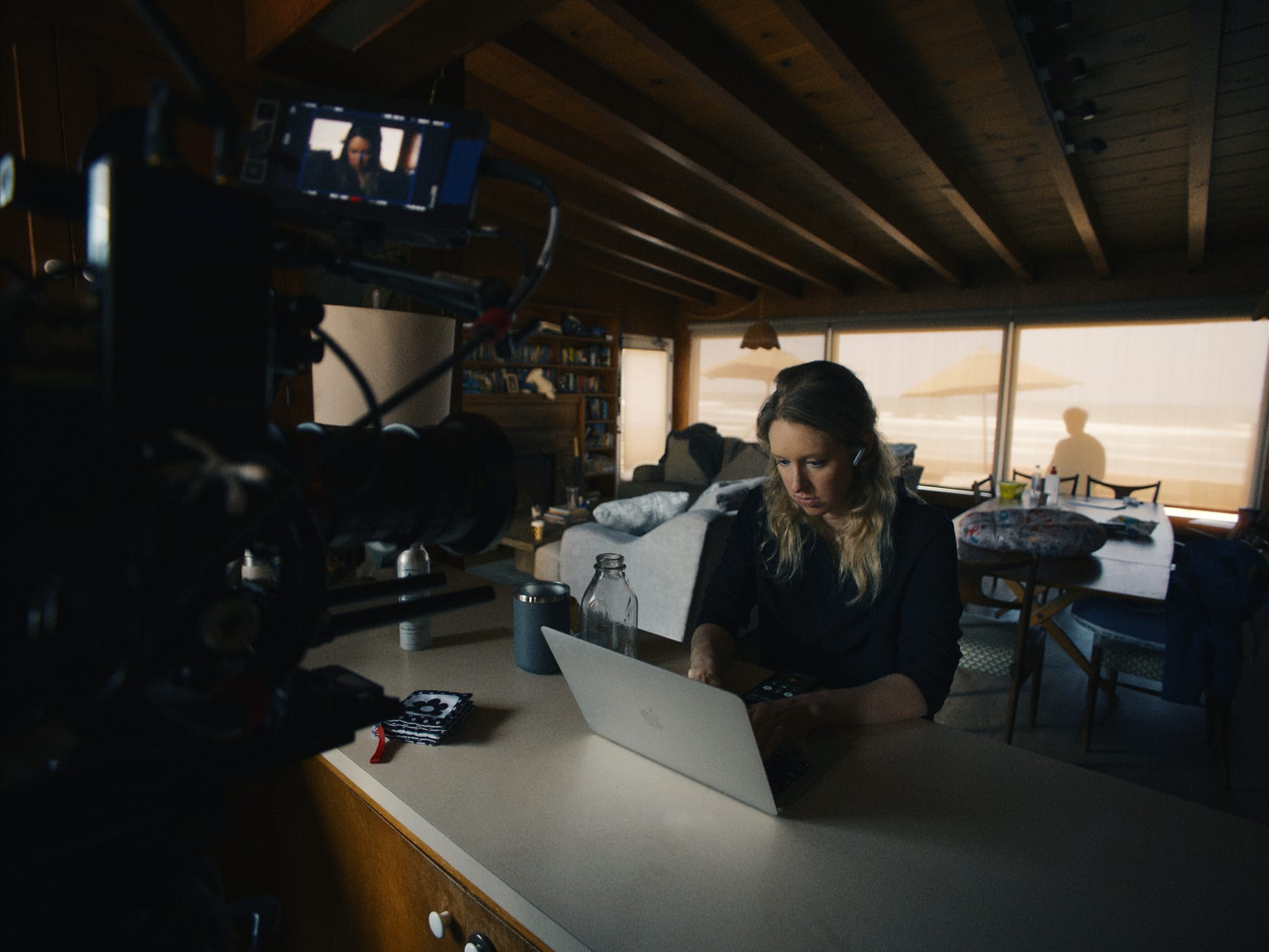 White woman using a laptop while a film camera is pointed at her face