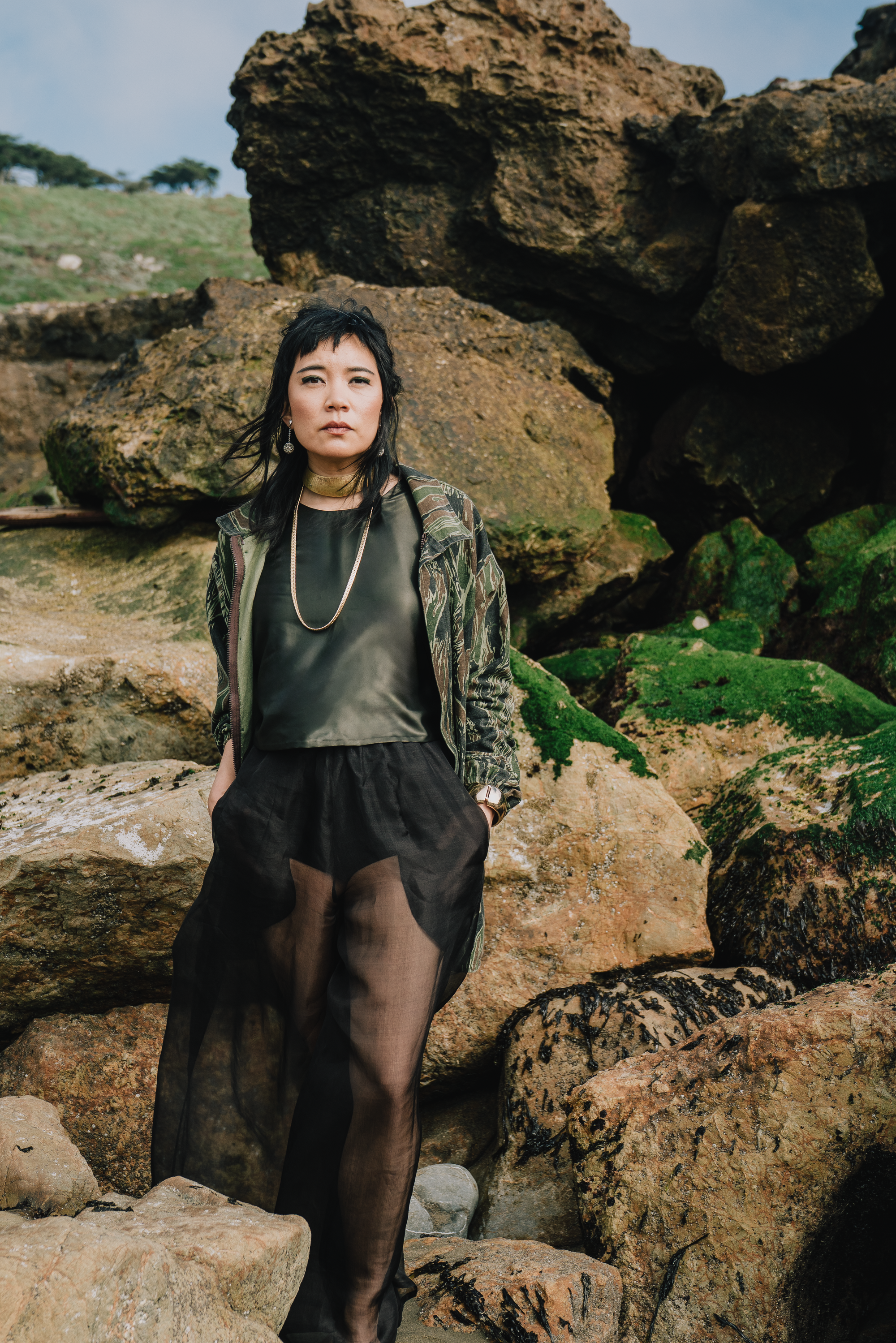 Woman in black clothing standing among rocks on a seashore.