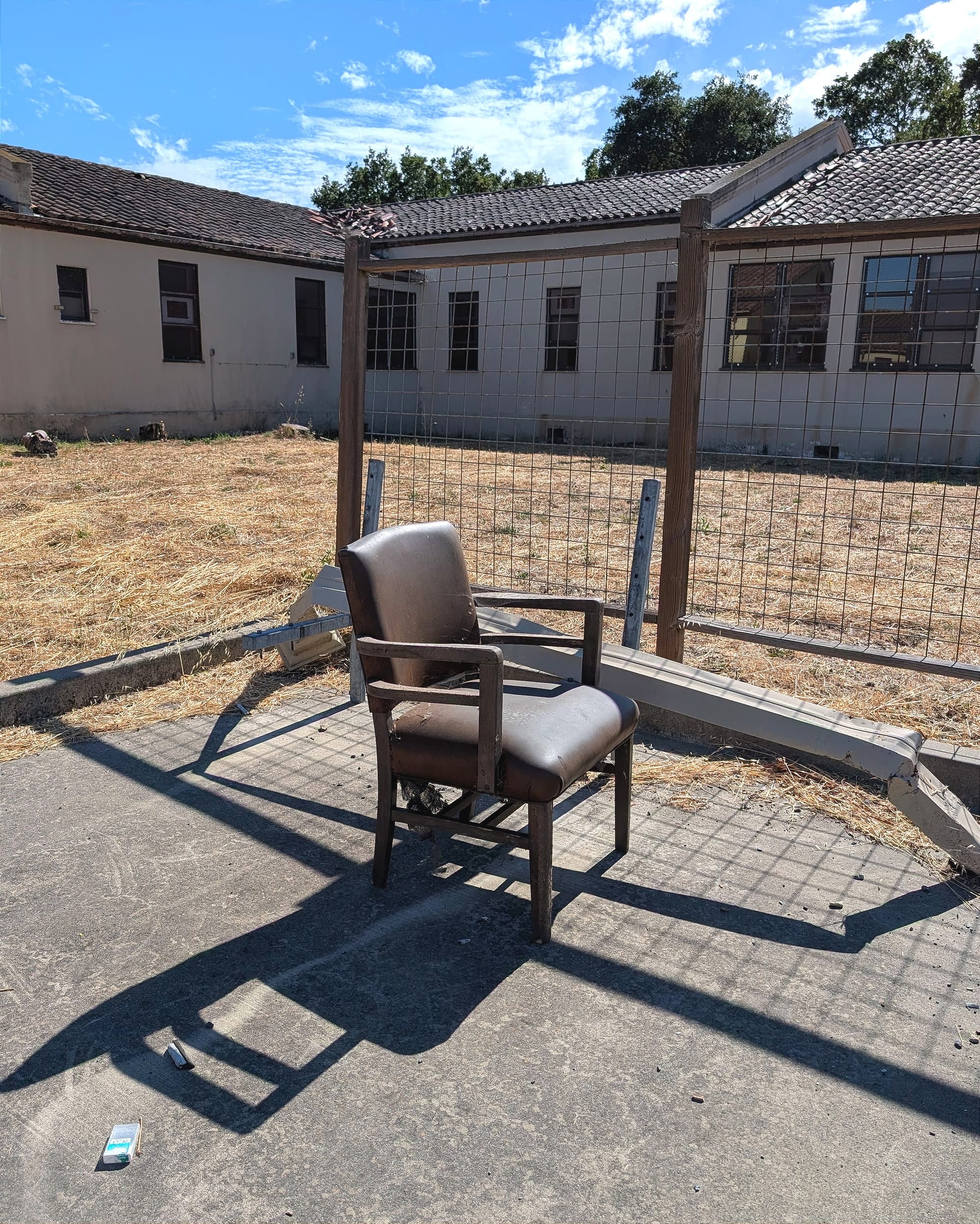 a chair outside an abandoned building with dead grass