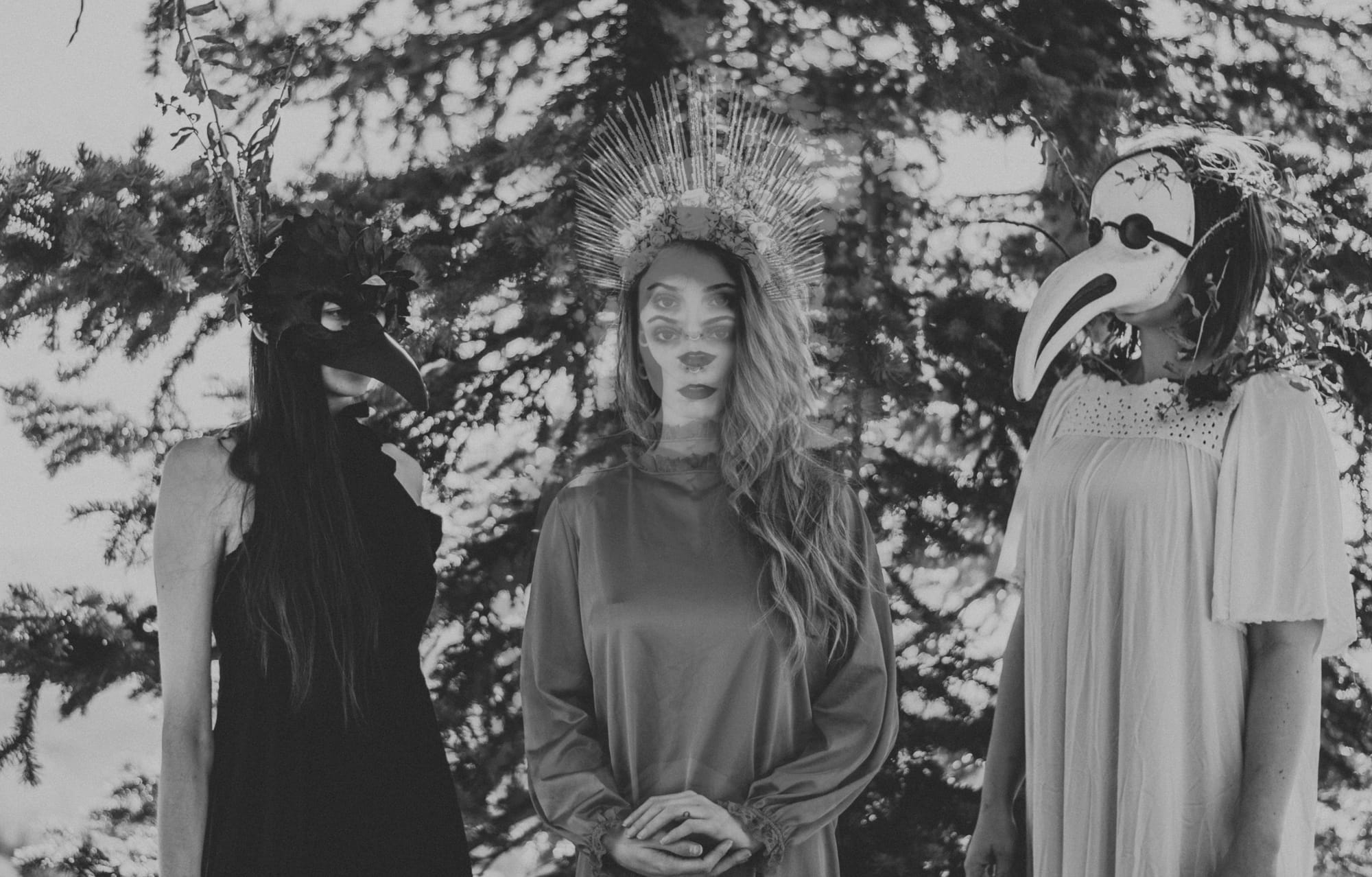 a spooky black and white photo of three women in costumes in the trees
