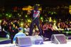 A man with dreadlocks stands on a stage in front of a crowd of people at night.