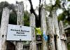 A mossy wooden fence with a small sign erected on it that says "Richard Bertram Barrett 'His Arm Lies Here'"