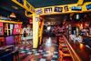 a colorful interior of a small music venue with a checkered floor, long wooden bar, and posters on the wall