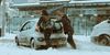 Two people pushing a car that's stuck in snow.
