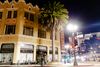 A night time photo of the Oakland School of the Arts building, which has brownish tan bricks and orange stars inlayed into the facade. There is a big palm tree in front of the building.