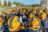 A group of football players in yellow helmets gathered around in a circle and getting excited.