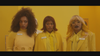 three Black women dressed all in yellow against a yellow wall, looking concerned and very cool