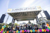 A band performs on an outdoor stage with a banner saying "Summer of Music"