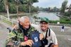 A smiling photo of a man and his grandfather holding the former’s debut poetry collection. Behind them is a lake. 