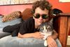 a curly-haired kid wearing sunglasses on a sofa with a grey and white cat