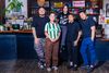 Five people in casual clothing standing together in front of a restaurant counter