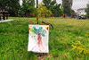 A sign hanging on a post in front of a sapling that depicts a marker-drawn image of a tree and text that says, "Bee nice to trees"