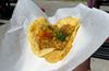 Trini doubles (two yellow bara on a parchment paper with stewed chickpeas and sauces on top)