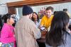 A masculine person holds a bag of coffee beans out toward a couple standing at a wooden counter.