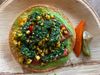 A tostada topped with green squash puree, chopped tomatoes, roasted corn kernels, and a salsa verde.