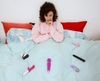 Woman in bed contemplating her collection of sex toys.