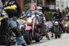 A person with pink hair and cat ears smiles as she rides a pink motorcycle in a crowd 
