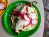 A roasted red pepper on a tortilla on a green plate, with green crema drizzled over it.