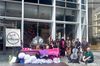 Group of people, many in brown robes, standing or sitting in front of an office building. A sign reads, "We Inter-Are."