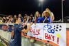 a women's soccer player signs an autograph for a young girl fan as lots of fans lean up against the railing at a Bay FC game with signs that show soccer balls and read "let's go bay FC"