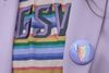 Closeup of a person wearing a lilac blazer over a rainbow t-shirt with a lavender lapel pin with a rainbow triangle logo