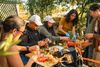 Five people chopping fruits and aromatics at a wooden table in a garden.