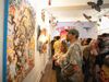 two people stand in front of colorful art in a gallery while other people smile around them at a gallery party