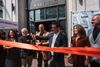 A row of people smile as a large red ribbon is cut in front of the Warfield Commons building. 