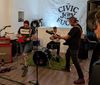 a punk trio wearing screenprinted masks perform a show in a small gallery