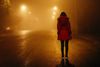 a person in a red jacket stands with her back to the camera on a foggy empty street at night