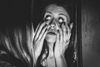 a black and white image of a woman with her hands on her face pulling her lower eyelids down in a creepy manner