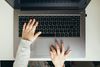a young child's hands are seen from above typing on a laptop keyboard
