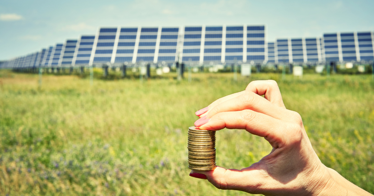  Mão segurando moedas com painéis solares ao fundo, simbolizando economia e sustentabilidade na energia renovável.