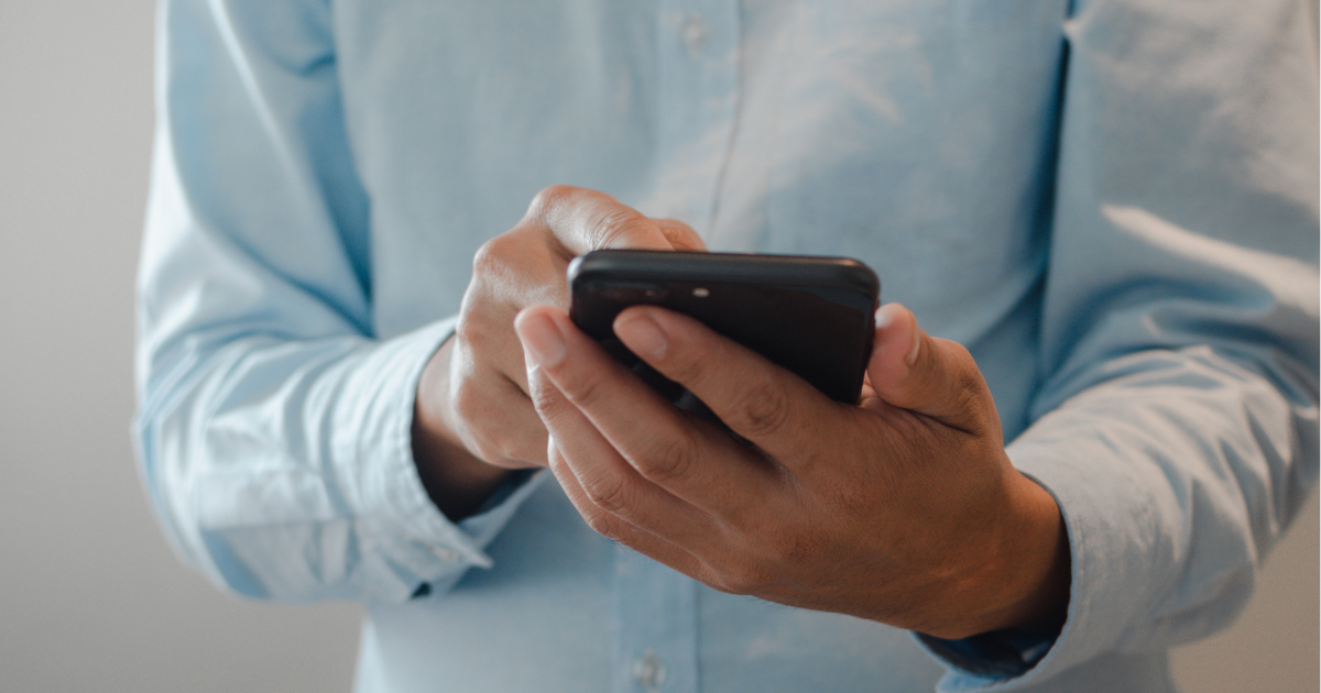 Pessoa usando um smartphone, vestindo uma camisa azul clara, em um ambiente interno.