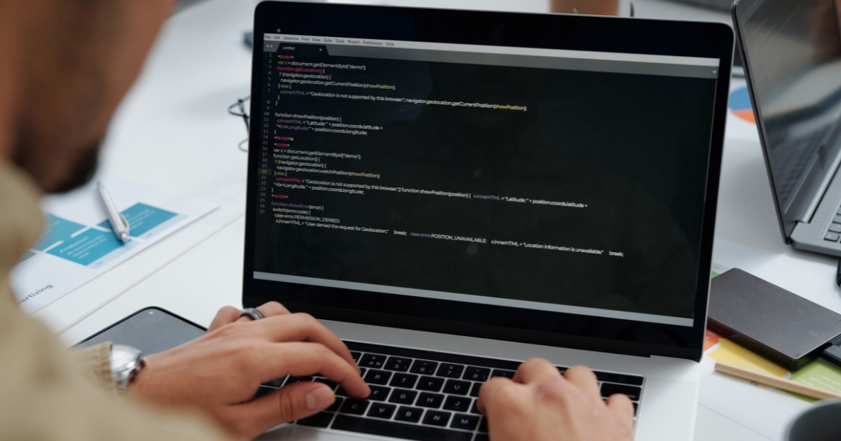 A imagem mostra uma pessoa digitando em um laptop com código exibido na tela. 