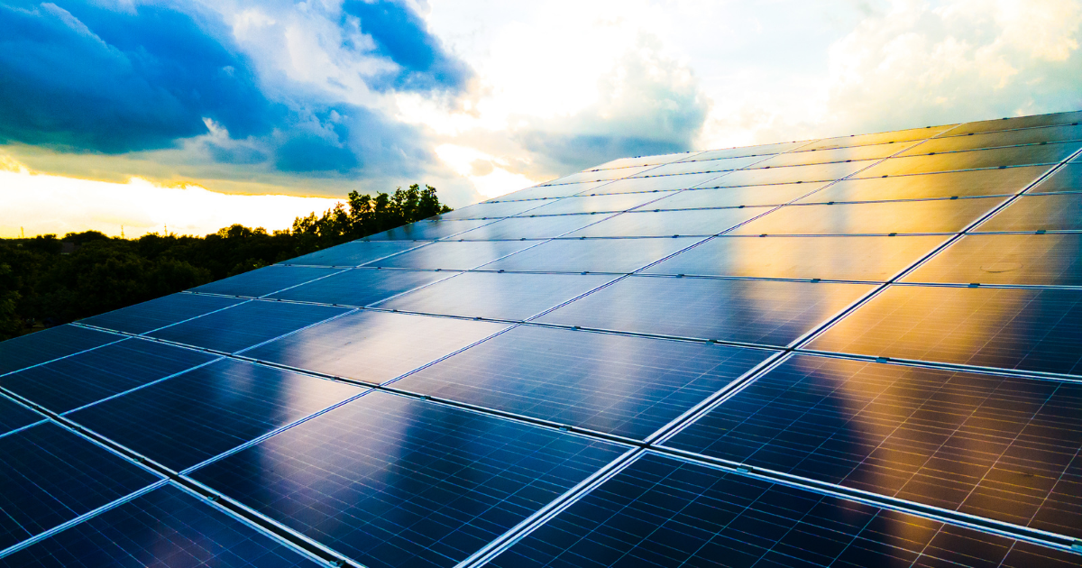 Painéis solares captam a luz do sol ao entardecer, refletindo o céu entre nuvens. Ideal para comunicar energia limpa e sustentabilidade.