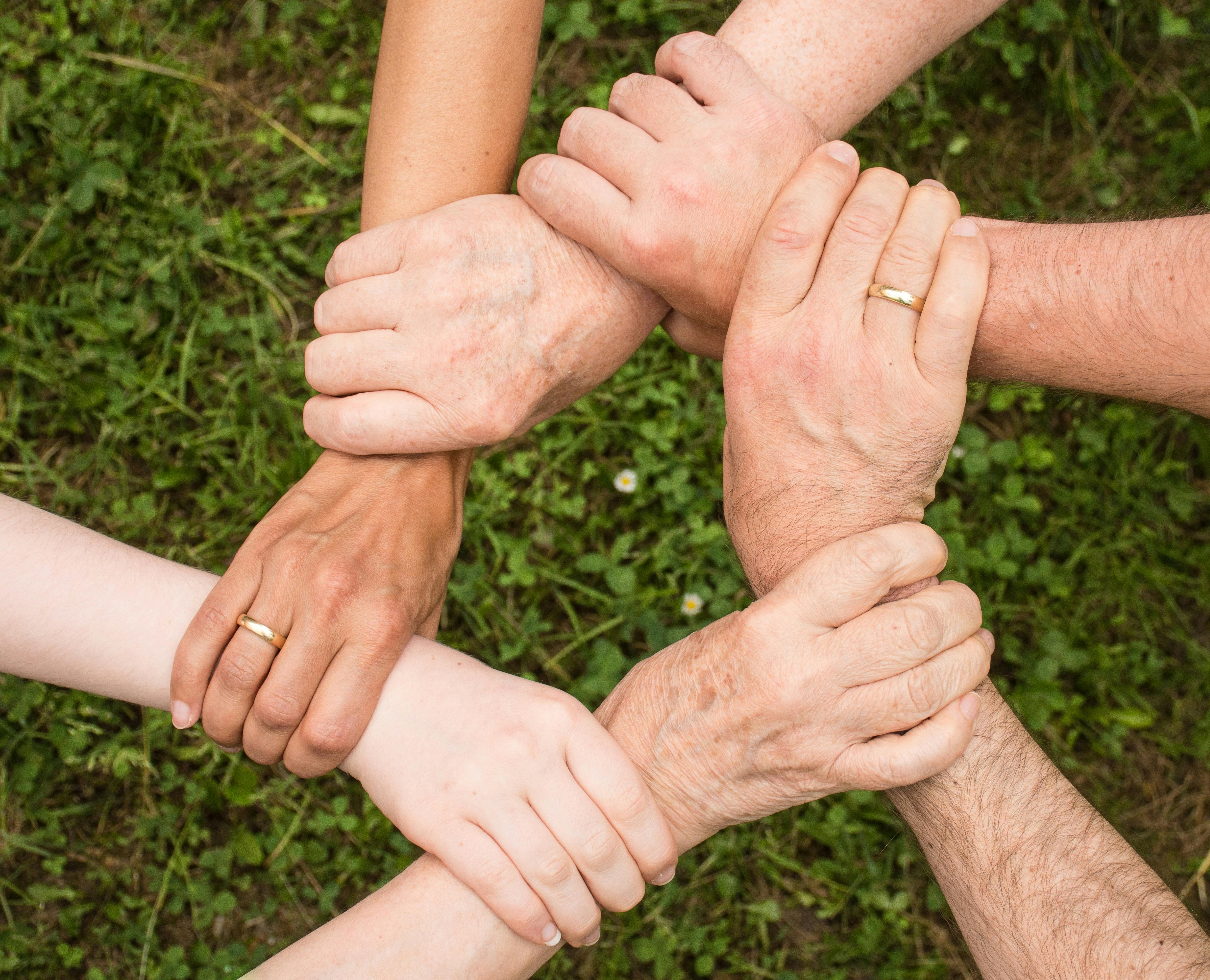 Six hands clasp another person's wrist, making a kind of circle of support