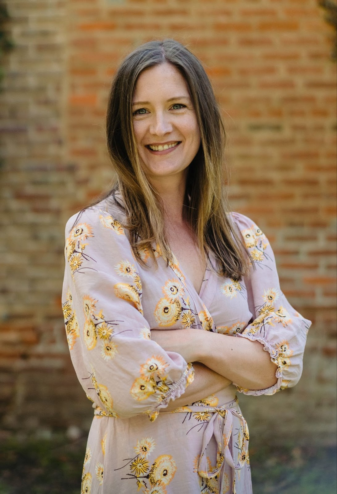 Sarah Ligon appears in a floral dress in front of a brick wall.